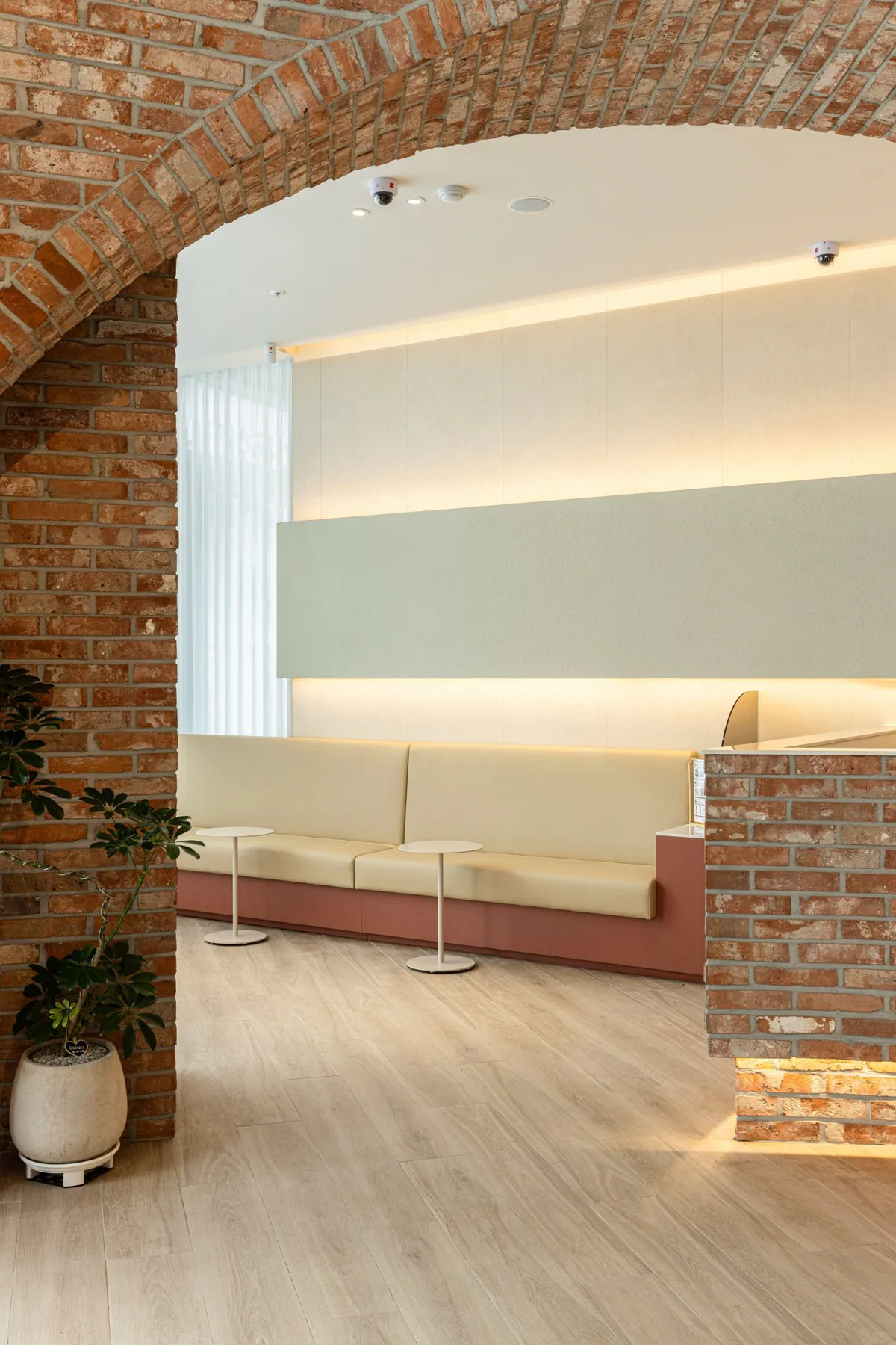 Waiting area seen through a brick arch, with a cream sofa and indirect lighting under a brick counter