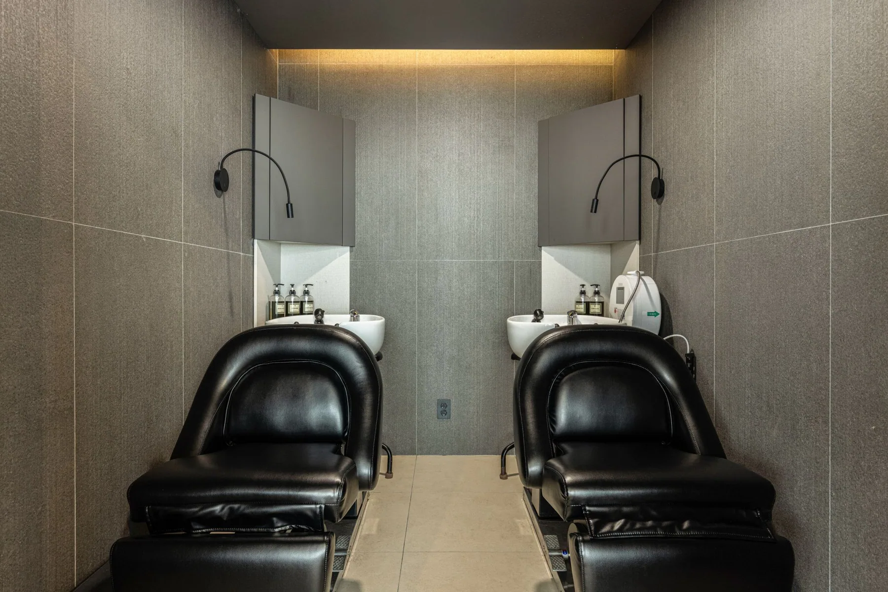 Two black shampoo chairs in front of a dark gray tiled wall